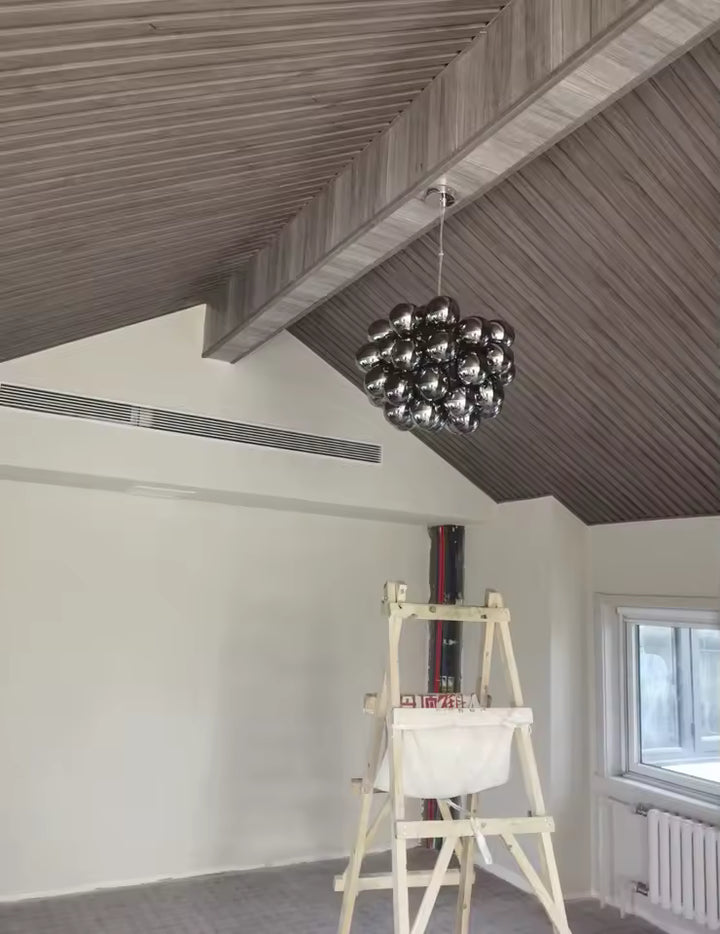 Sous un plafond en bois, ce lustre grappe en verre fumé affirme un style contemporain, graphique et sculptural