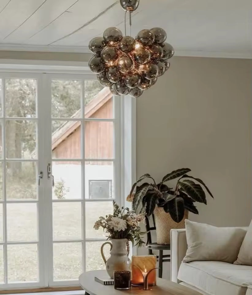 Suspendu dans un salon lumineux, ce lustre grappe en verre fumé apporte un style organique, élégant et contemporain