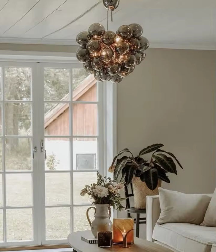 Suspendu dans un salon lumineux, ce lustre grappe en verre fumé apporte un style organique, élégant et contemporain