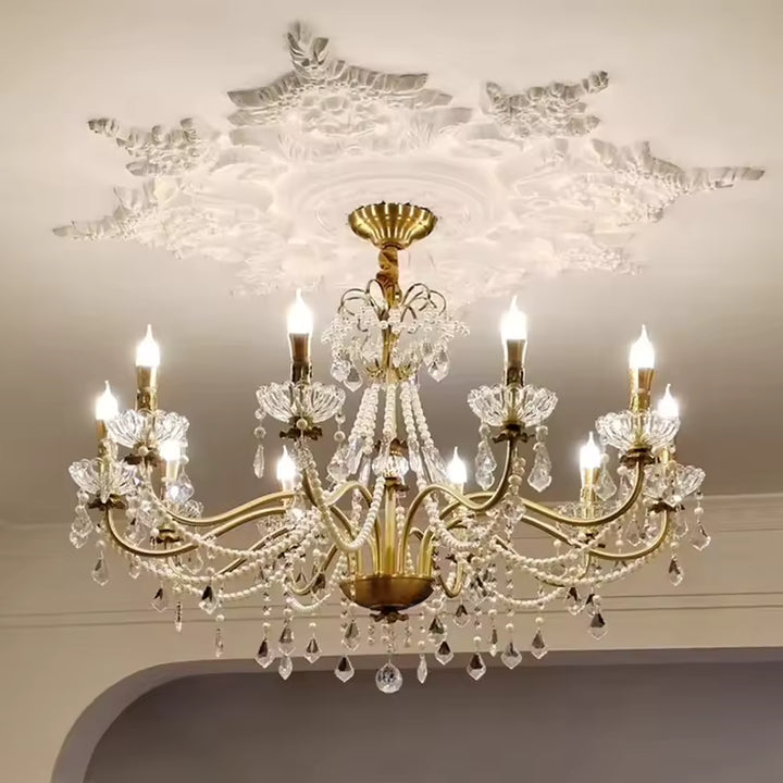 Sous un plafond sculpté, un lustre laiton vintage à pampilles en cristal et bras dorés sublime un décor majestueux.