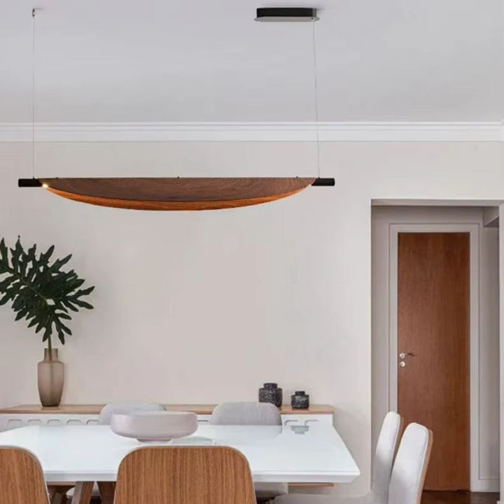 Dans une salle à manger épurée, le lustre en lame courbe effet bois souligne un style moderne, sobre et élégant