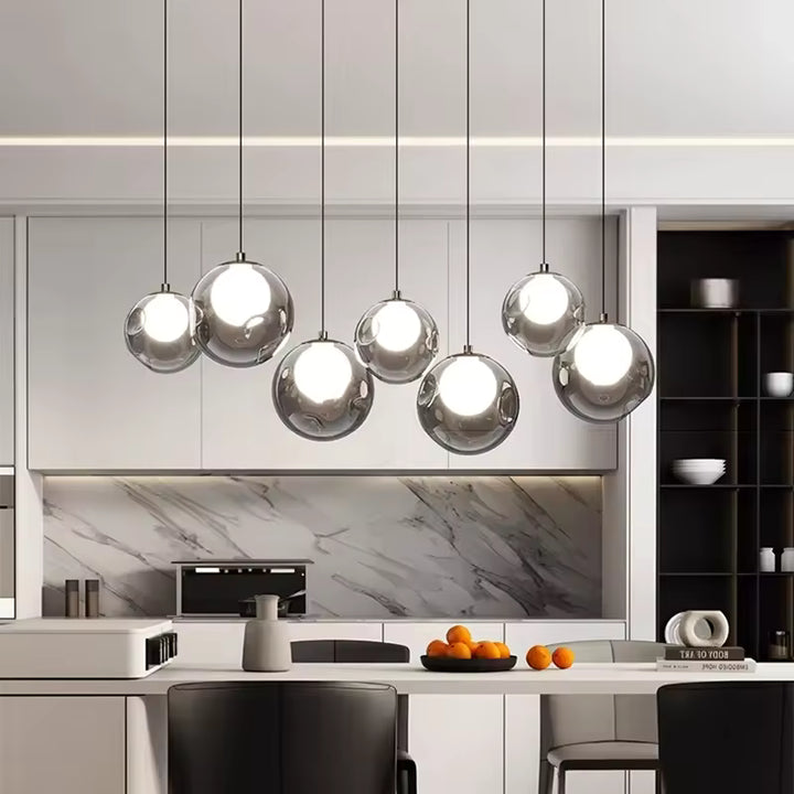 Au-dessus d'un îlot de cuisine contemporain, sept globes en verre transparent aux cœurs lumineux forment un lustre design.