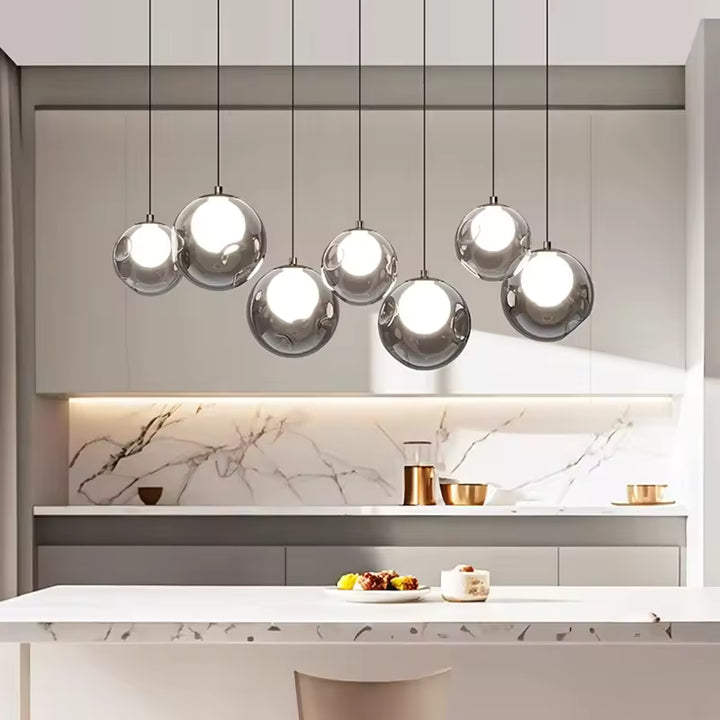 Alignement de sept globes en verre transparent à cœurs lumineux, suspendus au-dessus d'un îlot de cuisine au style épuré.