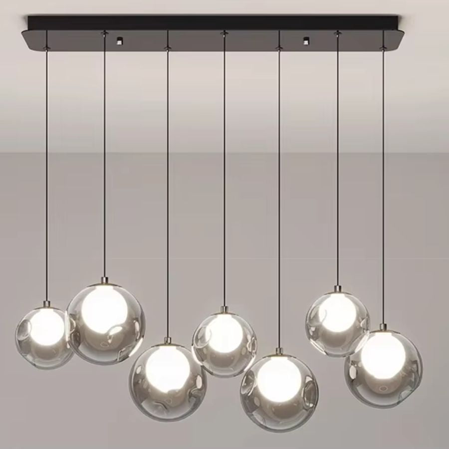 Vue frontale d'un lustre moderne à sept globes transparents et cœurs lumineux, suspendus en quinconce à une rosace noire.