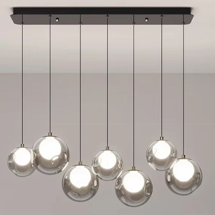Vue frontale d'un lustre moderne à sept globes transparents et cœurs lumineux, suspendus en quinconce à une rosace noire.