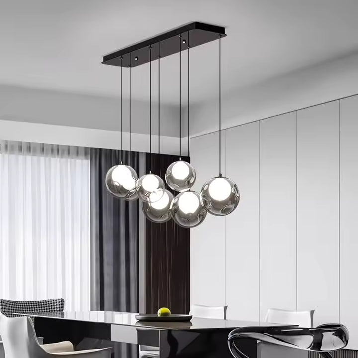 Au-dessus d'une table noire, un lustre contemporain à globes transparents et cœurs lumineux est suspendu à une barre noire.