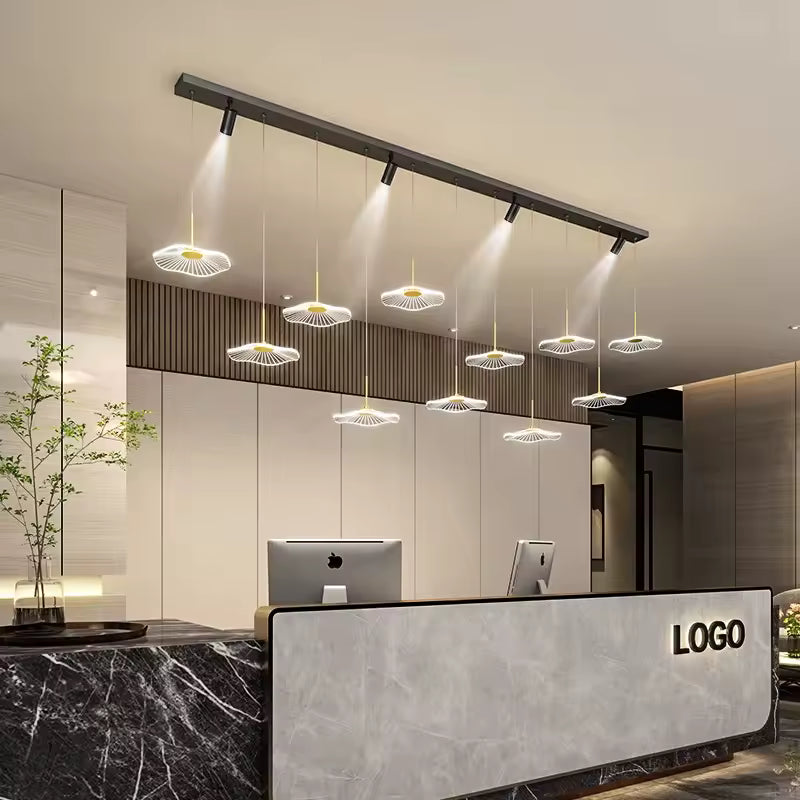 Un lustre contemporain à 11 ombrelles LED et quatre spots noirs orientables éclaire un comptoir de réception en marbre.