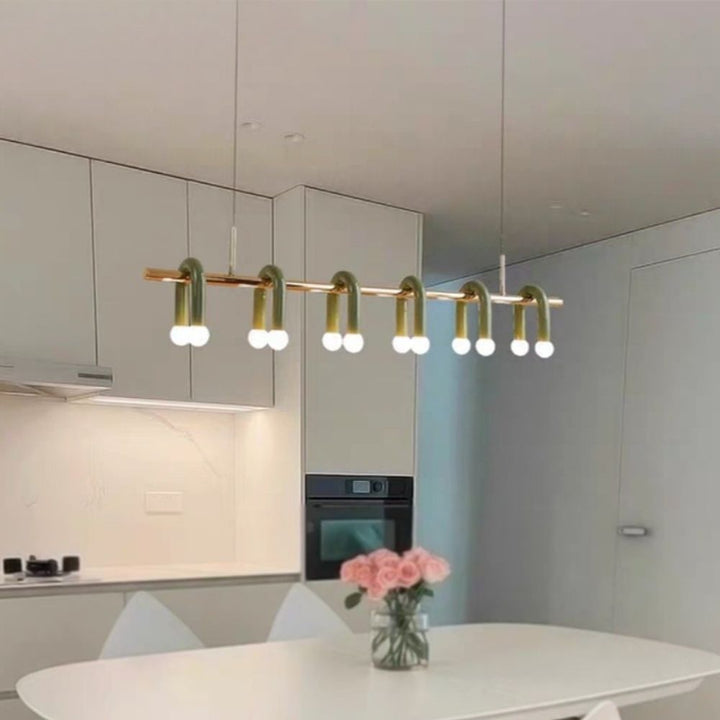 Lustre linéaire vert et doré intégré dans un espace de vie minimaliste et baigné de lumière.