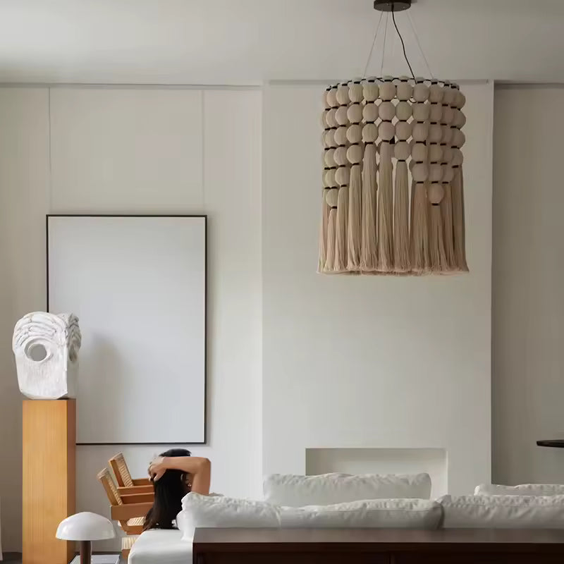 Lustre macramé à perles et longues franges en coton beige, suspendu dans un salon contemporain au décor minimaliste.
