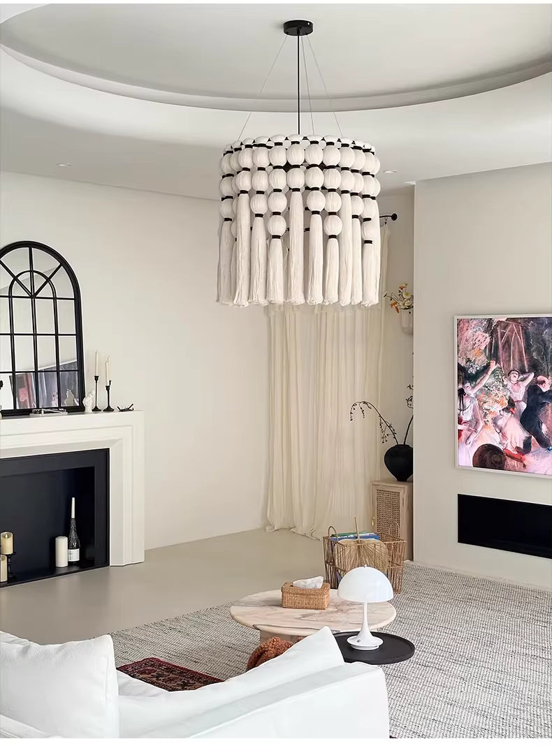 Un lustre macramé en coton écru à pompons et longues franges habille un salon élégant aux accents bohèmes.