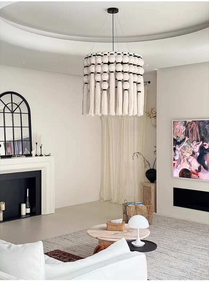 Un lustre macramé en coton écru à pompons et longues franges habille un salon élégant aux accents bohèmes.