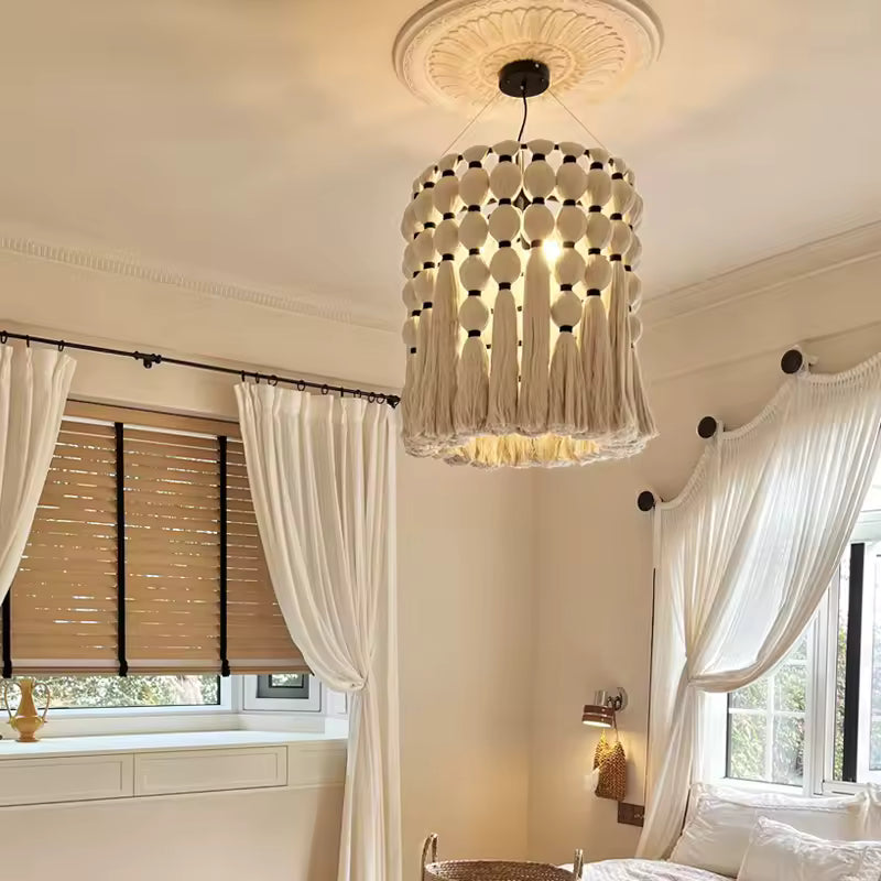 Lustre macramé en coton écru à pompons et franges, illuminant une chambre élégante aux accents bohèmes et classiques.