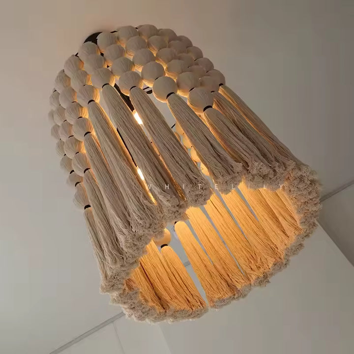 Lustre macramé bohème en coton beige, orné de perles et de longues franges diffusant une lumière chaude.