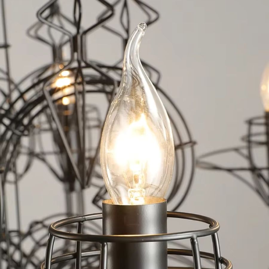 Détail d'une ampoule flamme allumée dans son support métallique ajouré, sur un lustre noir baroque aux accents gothiques.