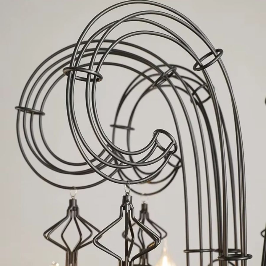 Gros plan sur les volutes spiralées en métal noir d'un lustre baroque, ornées de pampilles filaires au charme néogothique.