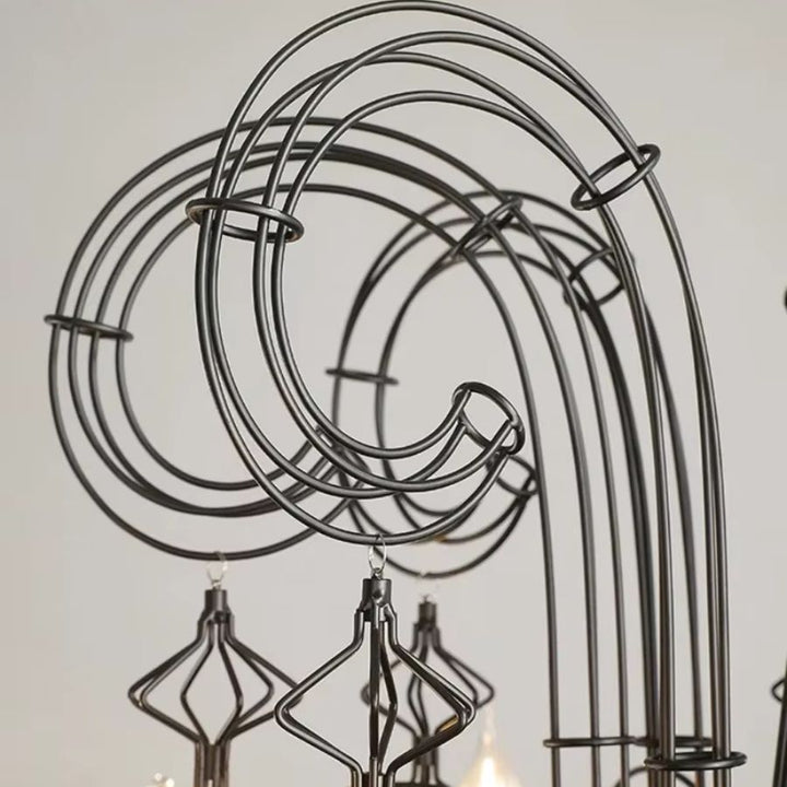 Gros plan sur les volutes spiralées en métal noir d'un lustre baroque, ornées de pampilles filaires au charme néogothique.