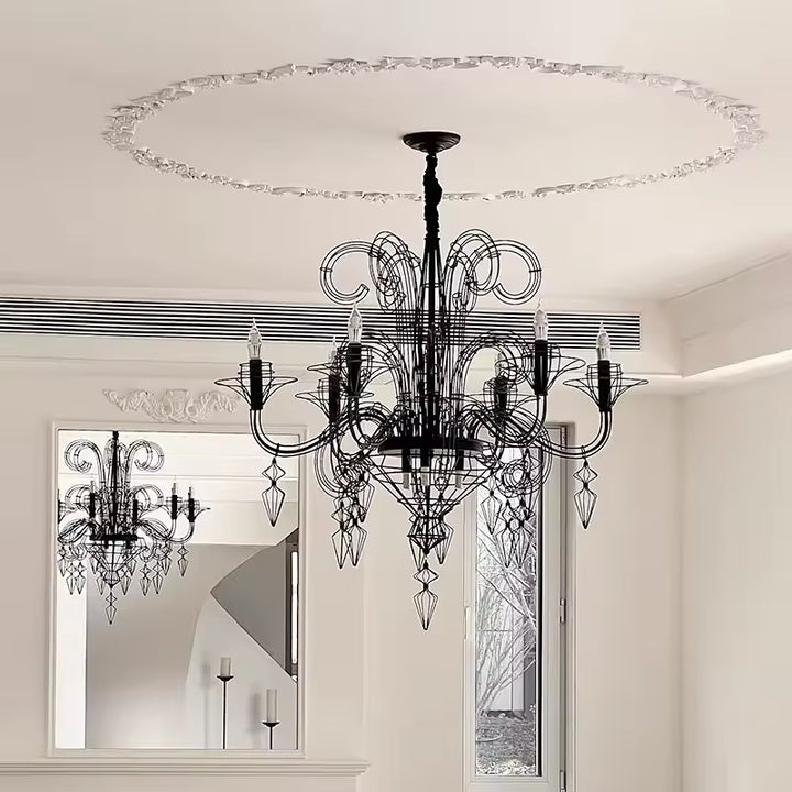 Sous un plafond à moulures, lustre noir baroque à volutes filaires et pampilles suspendues, au charme néoclassique.