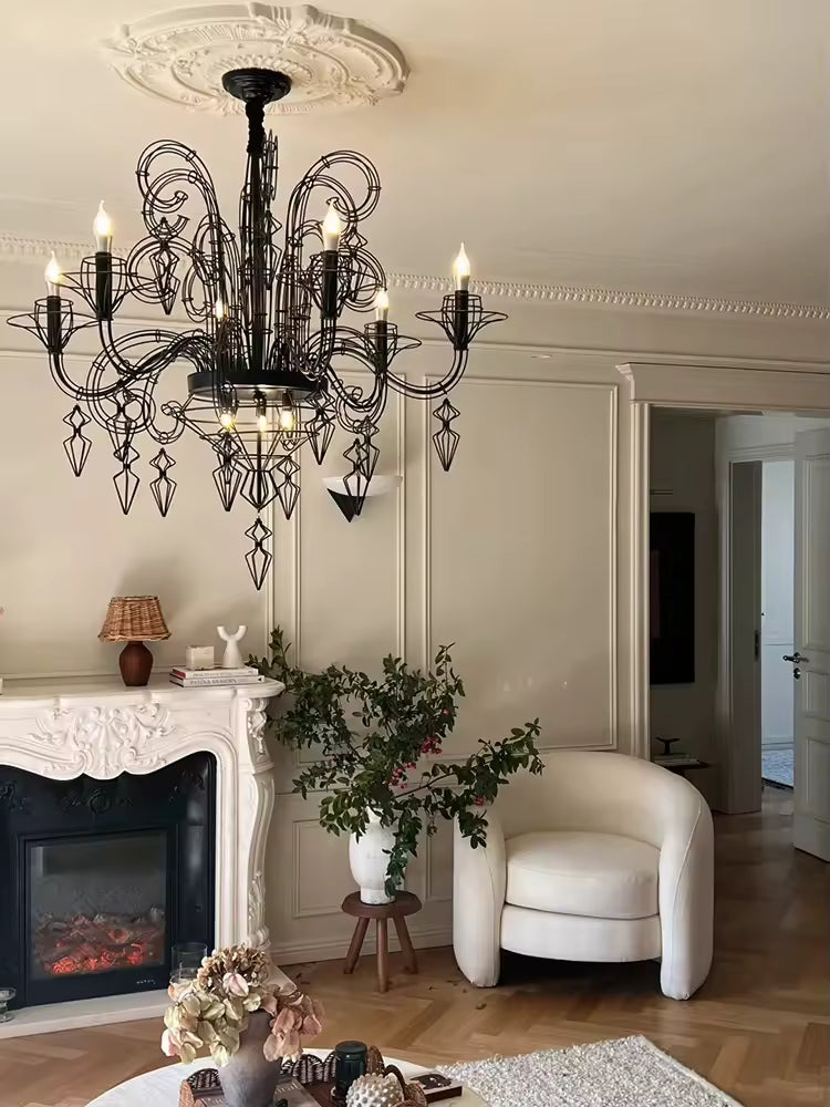 Dans un salon raffiné avec cheminée, lustre noir baroque à volutes métalliques et pampilles ajourées, d'esprit néoclassique.