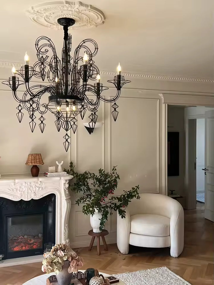 Dans un salon raffiné avec cheminée, lustre noir baroque à volutes métalliques et pampilles ajourées, d'esprit néoclassique.