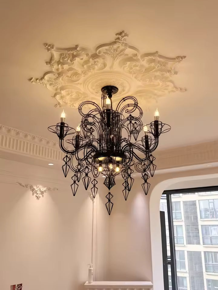 Éclairé d'une lumière chaleureuse, ce lustre noir baroque aux volutes métalliques contraste avec une rosace sculptée.