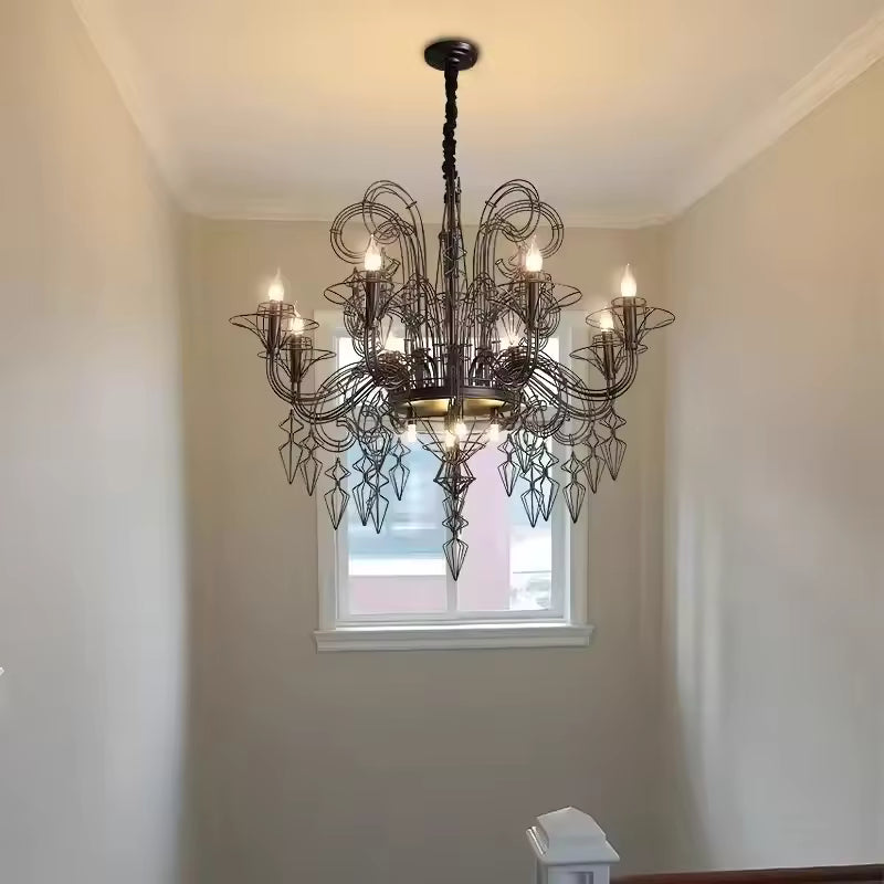 Dans une cage d'escalier lumineuse, lustre noir baroque à volutes métalliques et pampilles géométriques, d'esprit gothique.