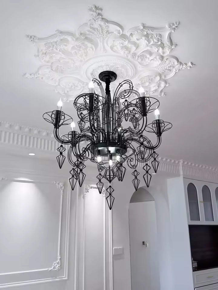 Fixé sous une rosace sculptée, ce lustre noir baroque aux volutes ajourées et pampilles filaires offre un contraste élégant.