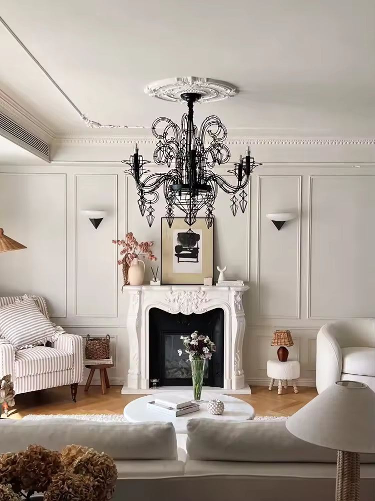 Au-dessus d'une cheminée ancienne, lustre noir baroque à volutes ajourées et pampilles filaires, au charme classique chic.