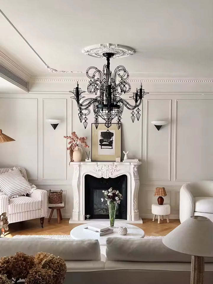 Au-dessus d'une cheminée ancienne, lustre noir baroque à volutes ajourées et pampilles filaires, au charme classique chic.