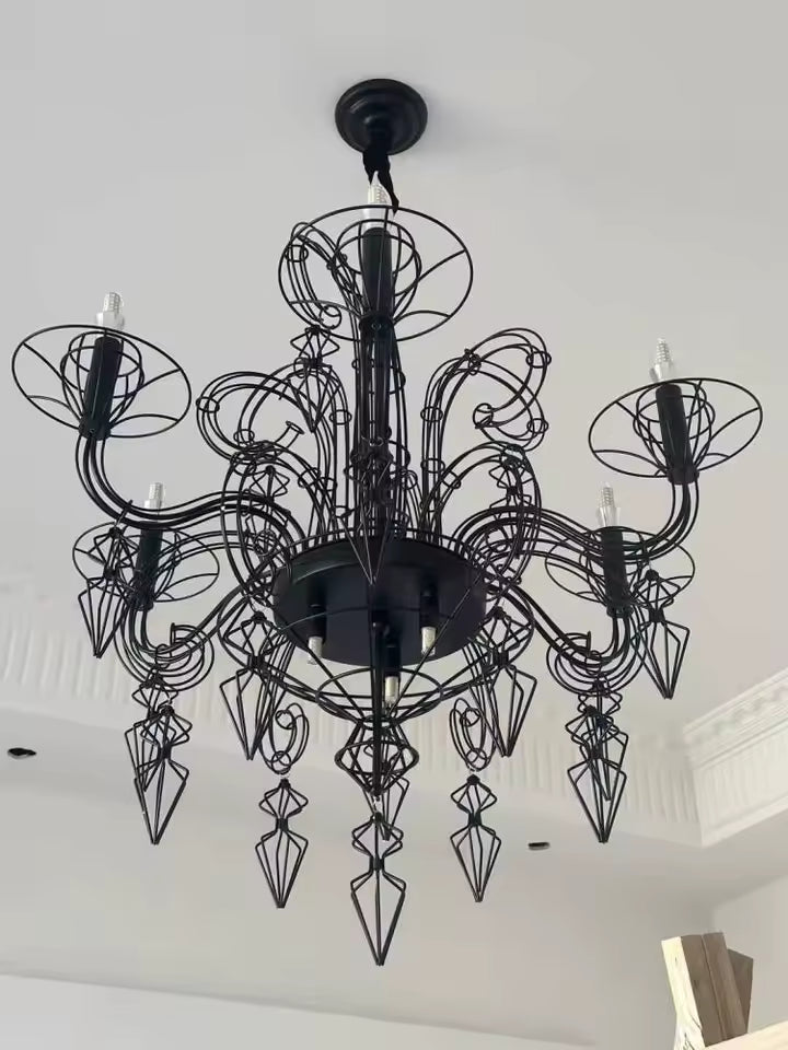 Vue de dessous d'un lustre noir baroque aux bras courbés, volutes métalliques et pampilles ajourées d'esprit néogothique.