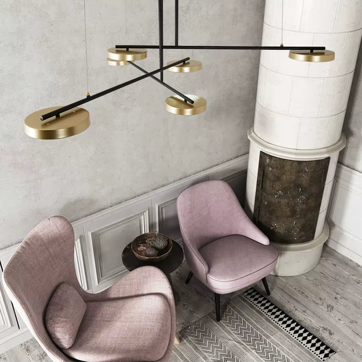 Au-dessus d’un coin salon, ce lustre noir et doré aux bras croisés apporte une touche rétro moderne et sculpturale.