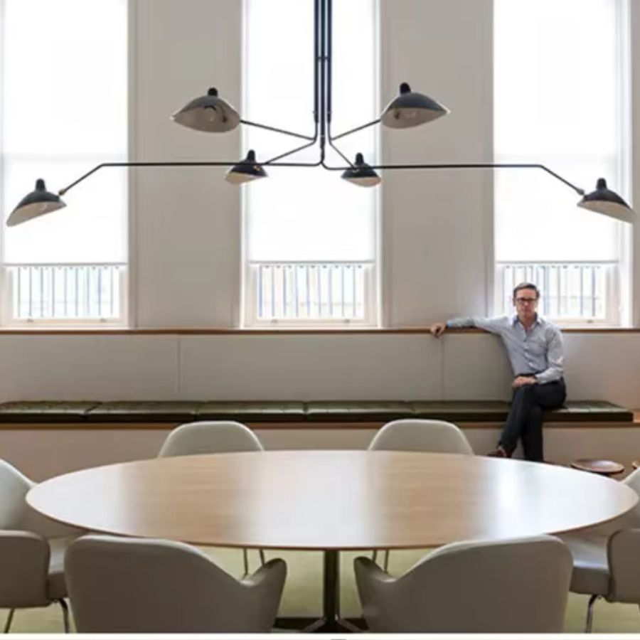 Dans une salle de réunion lumineuse, grand lustre noir à six coupoles métalliques et bras déployés, d'inspiration mid-century.