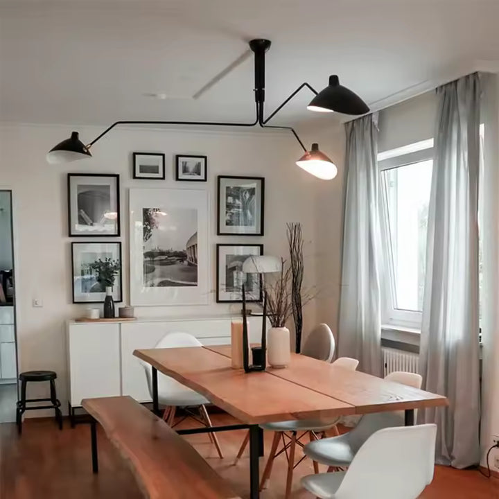 Au-dessus d'une table en bois, lustre noir à bras articulés et trois coupoles métalliques, d'inspiration rétro et industrielle.