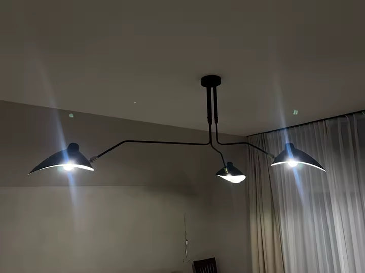 Éclairé dans une pièce tamisée, ce lustre noir à trois coupoles et bras étirés révèle son allure rétro industrielle.