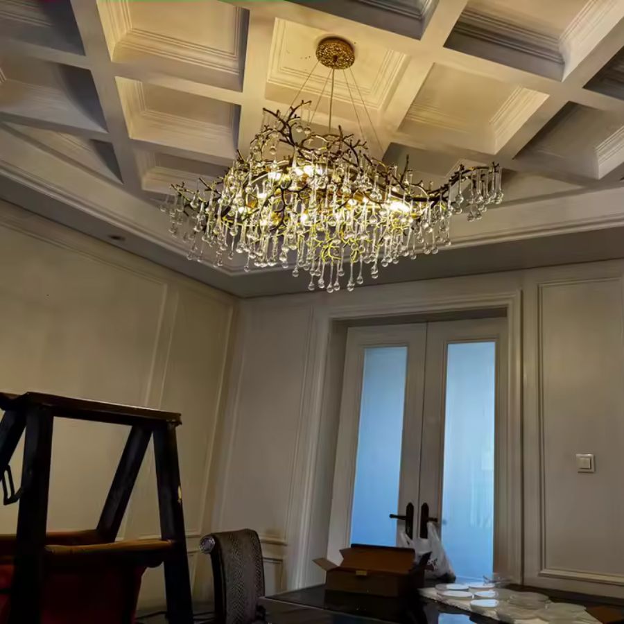 Sous un plafond à caissons, ce lustre à pampilles de cristal et branches dorées apporte une élégance classique et sculpturale