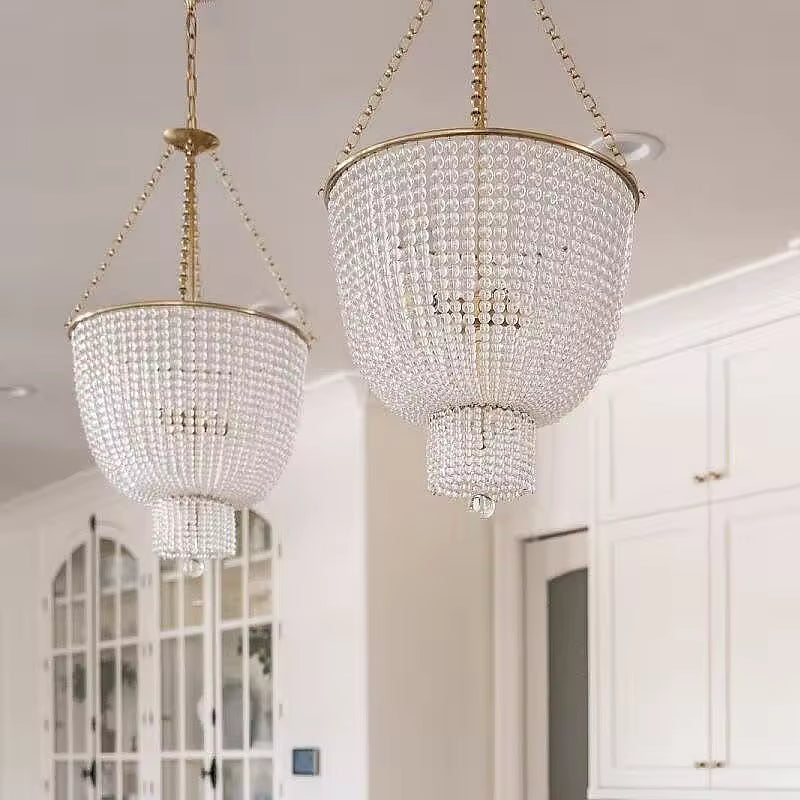 Deux lustres à perles de cristal en cascade, aux montures dorées de style Art déco, éclairant une cuisine élégante.