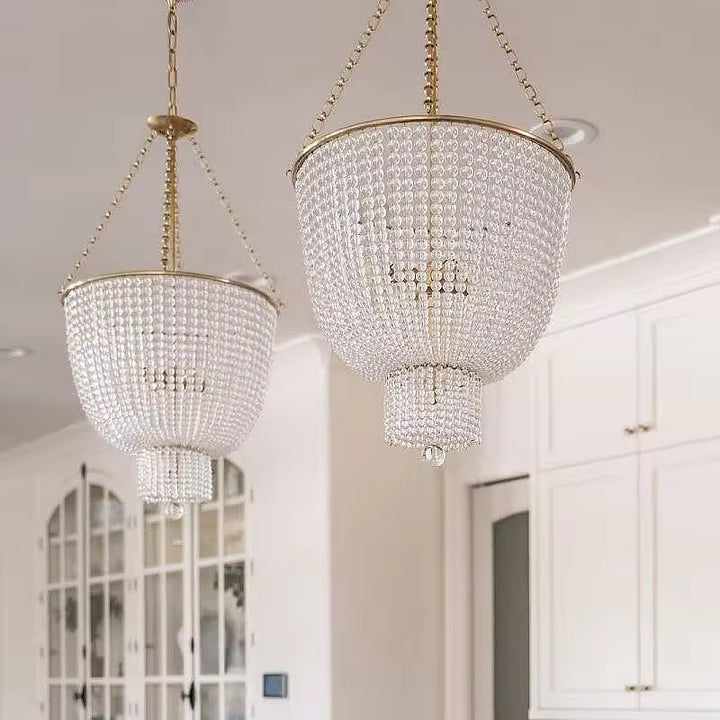 Deux lustres à perles de cristal en cascade, aux montures dorées de style Art déco, éclairant une cuisine élégante.