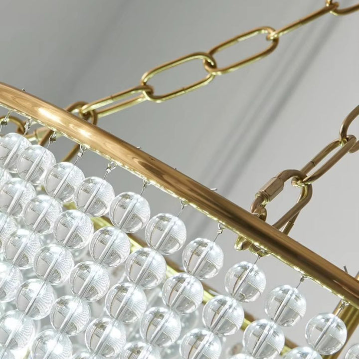 Détail des chaînes dorées et des rangées de perles transparentes d'un lustre à perles au design Art déco raffiné.