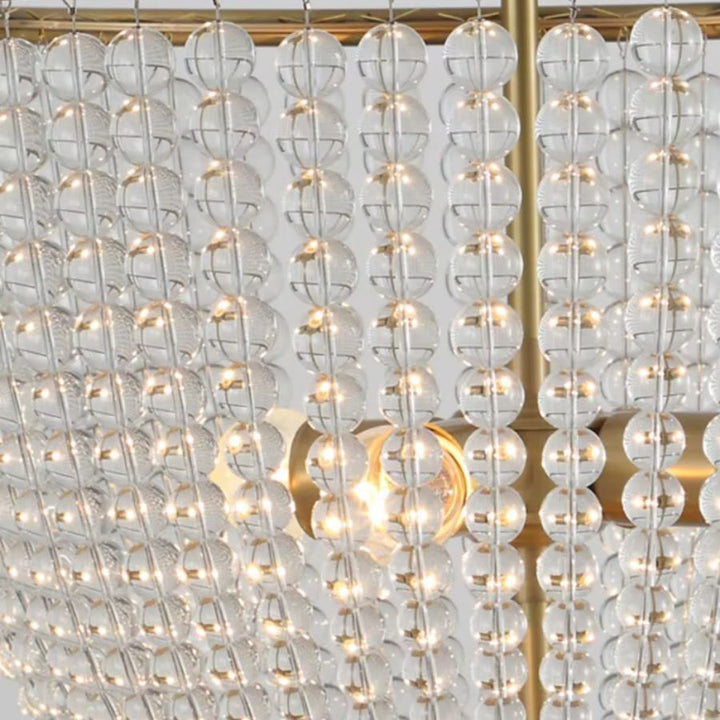 Gros plan sur les rangées de perles de cristal transparentes d'un lustre à perles au style Art déco et finition dorée.