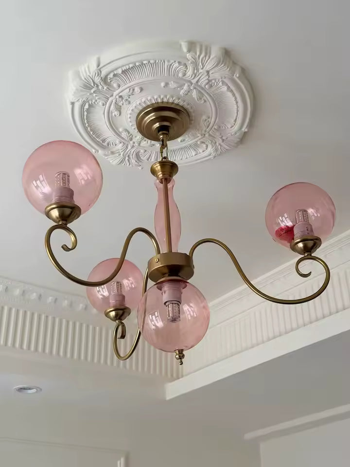 Lustre rose à globes en verre et bras dorés courbés, installé sous une rosace de plafond au style classique raffiné