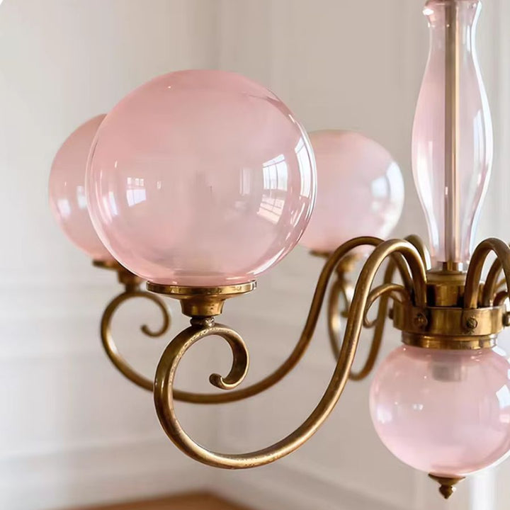 Détail d’un lustre rose poudré avec globe en verre et volute dorée, au style rétro chic et délicatement romantique