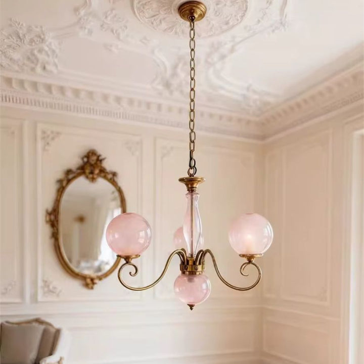 Lustre rose poudré à globes en verre suspendu par chaîne dorée, dans un intérieur classique au charme rétro raffiné