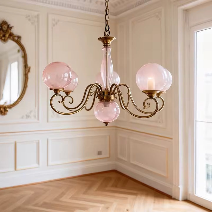Lustre à globes en verre rose poudré sur volutes dorées, dans un décor classique élégant aux notes rétro