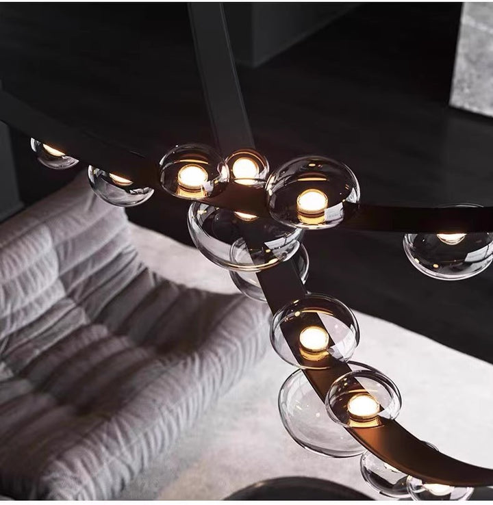 Lustre contemporain à ruban en cuir foncé et boules de verre lumineux dans un intérieur design et épuré.