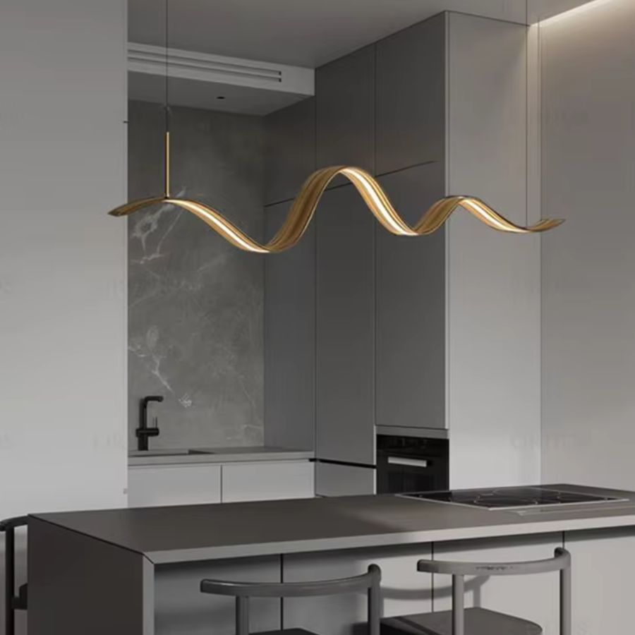 Dans une cuisine épurée, ce lustre ruban doré déploie une silhouette ondulée et sculpturale au-dessus de l’îlot