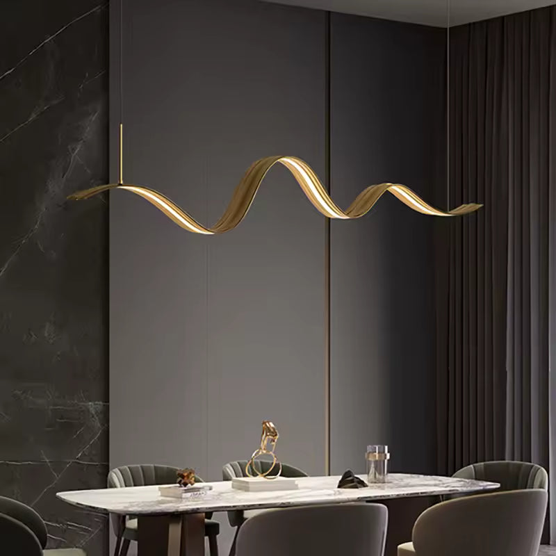 Au-dessus de la table, ce lustre ruban LED ondulé à finition dorée signe une présence sculpturale et contemporaine