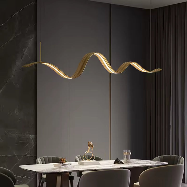 Au-dessus de la table, ce lustre ruban LED ondulé à finition dorée signe une présence sculpturale et contemporaine