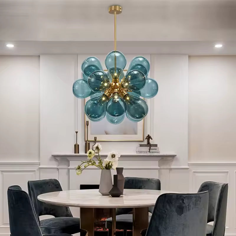 Lustre sculptural à 18 globes en verre bleu transparent et métal doré, au style vintage chic, suspendu dans une salle à manger.