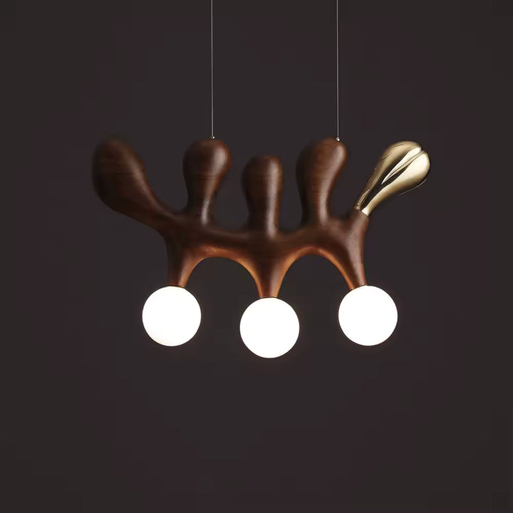 Sur fond sombre, ce luminaire sculptural en bois foncé révèle trois globes blancs et une silhouette organique