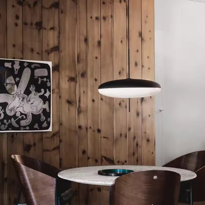 Lustre soucoupe noir et blanc au design moderne, suspendu au-dessus d’une table dans une salle à manger chaleureuse