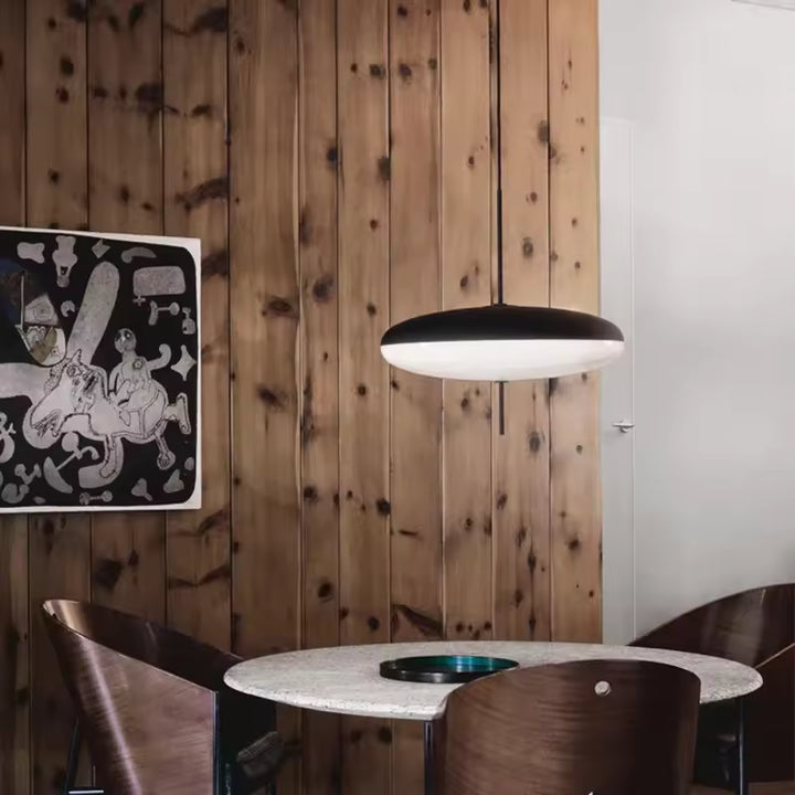 Lustre soucoupe noir et blanc au design moderne, suspendu au-dessus d’une table dans une salle à manger chaleureuse